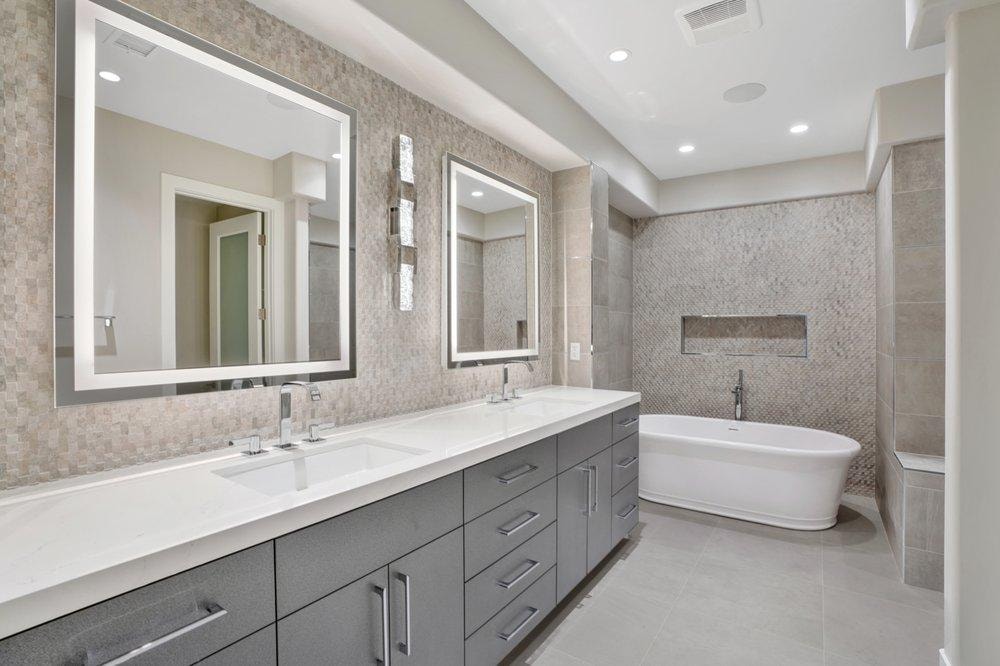 Bathroom remodel in Newport Beach CA — double vanity with quartz countertop, LED backlit mirrors, freestanding soaking tub, mosaic accent tile wall, and large format floor tile by Main Street Kitchen & Flooring