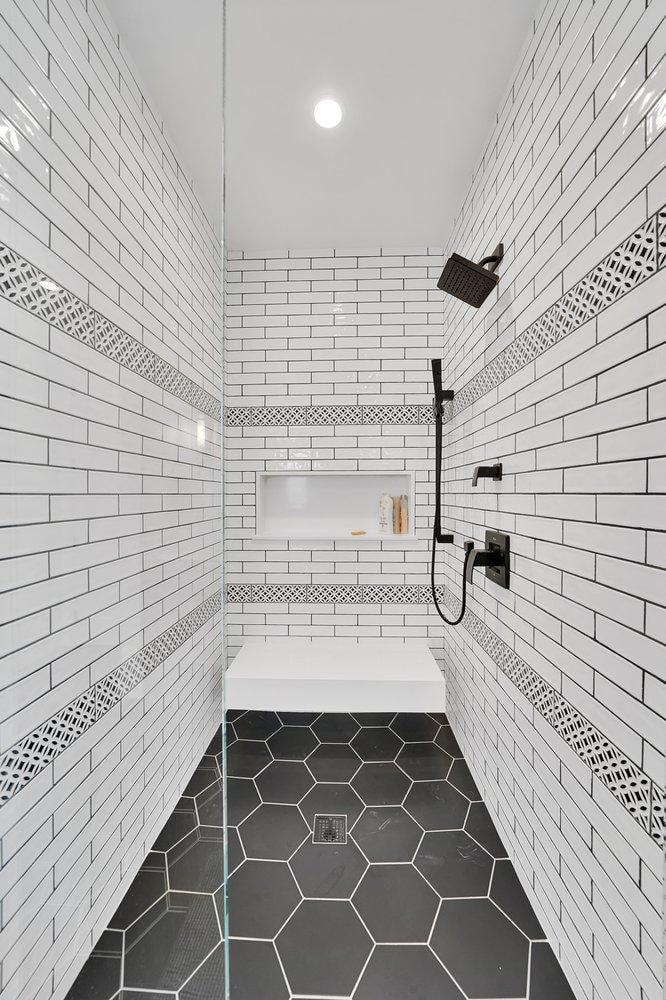 Bathroom remodel in Newport Beach CA — walk-in shower with white subway tile, decorative border tile, black matte fixtures, built-in bench, and black hexagon floor tile by Main Street Kitchen & Flooring