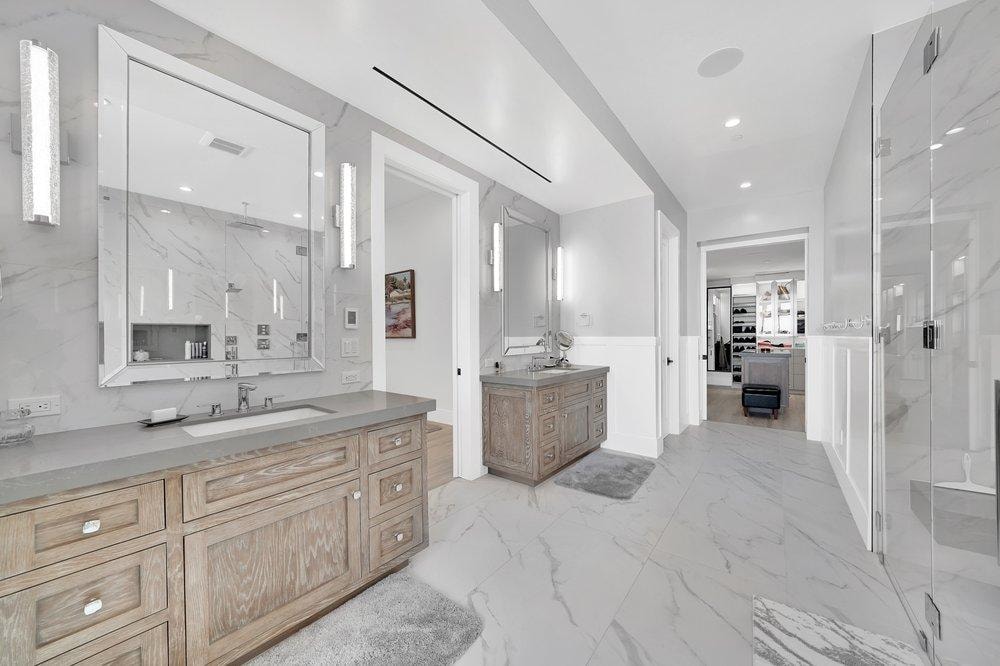 Bathroom remodel in Newport Coast CA — dual wood vanity with gray quartz countertop, full-height marble tile walls, frameless glass shower enclosure, and large format marble porcelain flooring by Main Street Kitchen & Flooring