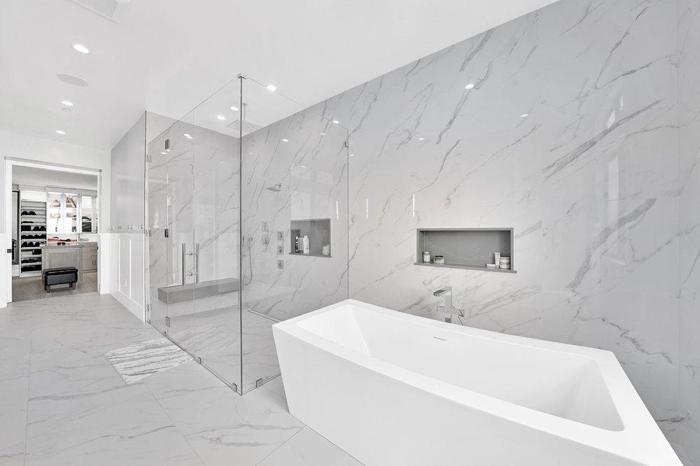 Bathroom remodel in Newport Coast CA — freestanding soaking tub, floor-to-ceiling marble slab walls, frameless glass walk-in shower with built-in niche, and large format marble tile flooring by Main Street Kitchen & Flooring