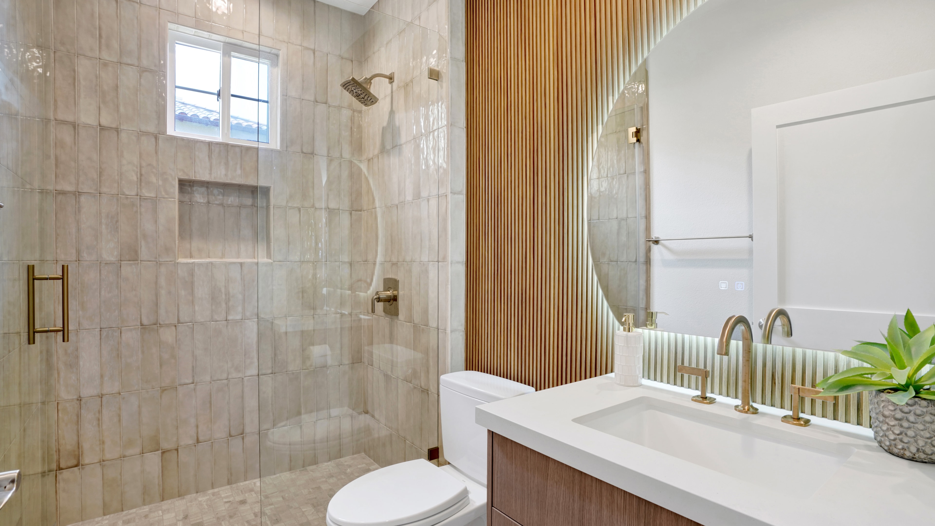 Bathroom remodel in Santa Ana CA — zellige ceramic tile walk-in shower with brass fixtures and niche shelf, wood slat accent wall, floating wood vanity with white quartz countertop, and round mirror by Main Street Kitchen & Flooring