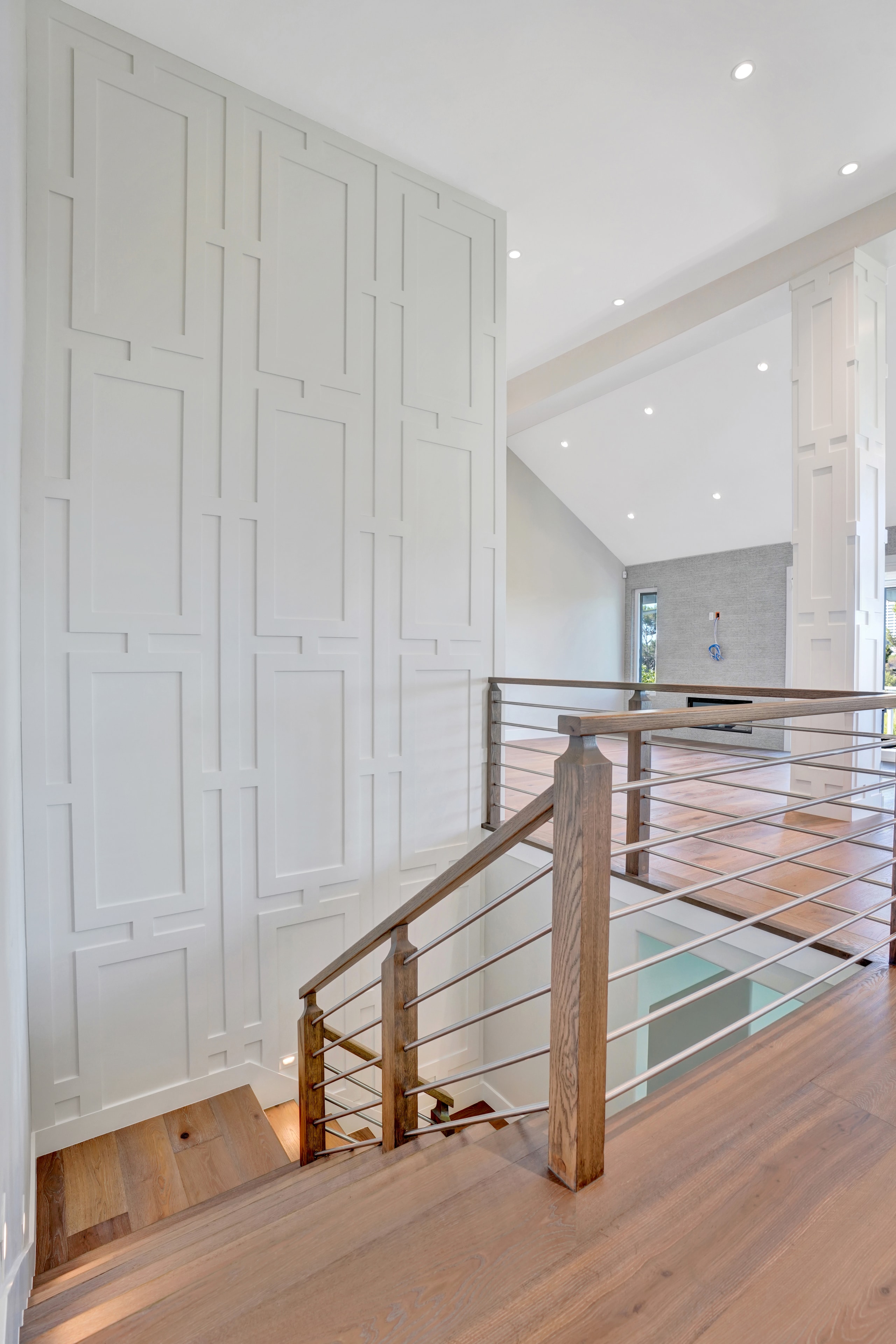 Home remodel in Orange County CA — staircase landing with custom geometric wainscoting wall panels, wood and stainless steel railing, and wide-plank hardwood flooring by Main Street Kitchen & Flooring