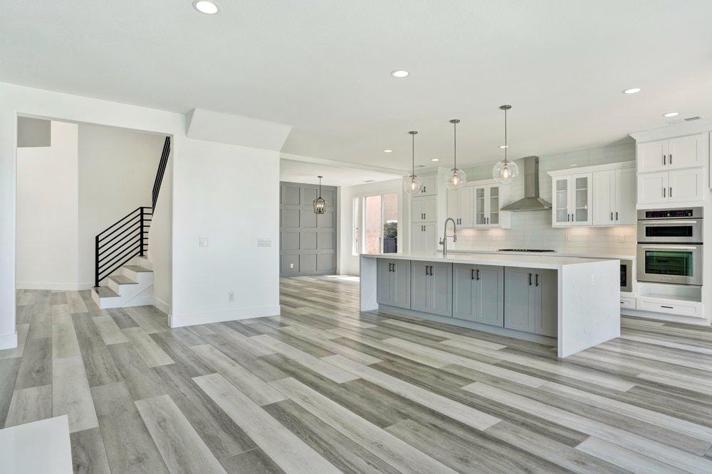 Open-plan kitchen remodel in Irvine CA — gray vinyl plank flooring, white shaker cabinets, and modern island with glass pendants by Main Street Kitchen & Flooring