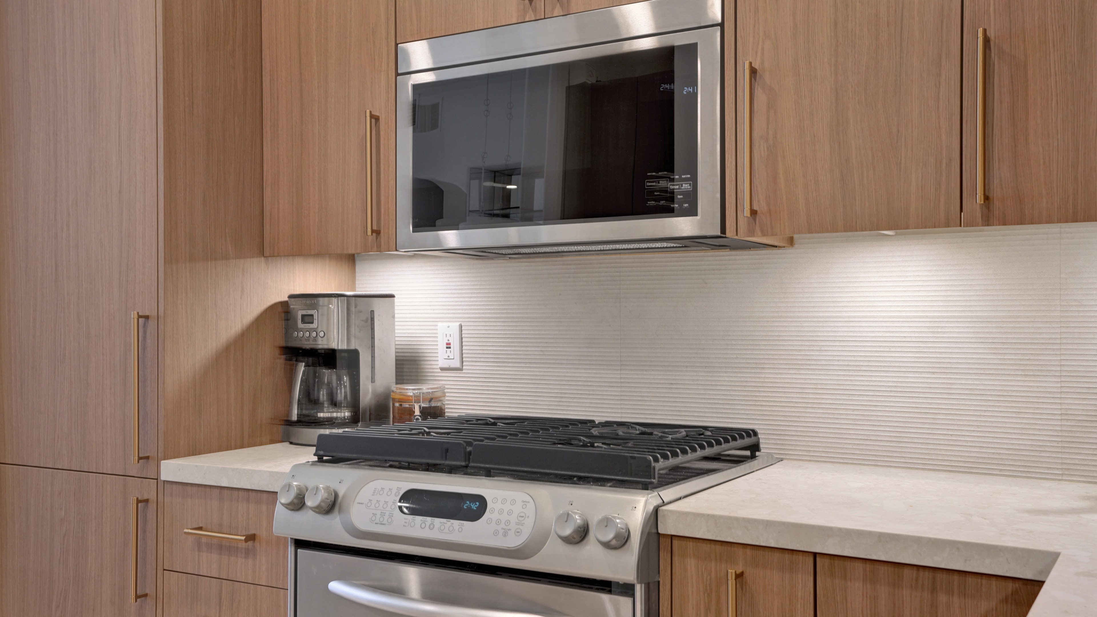 Kitchen remodel in Irvine CA — wood flat-panel cabinetry with brass pulls, stainless steel gas range with over-range microwave, fluted ceramic tile backsplash with under-cabinet lighting, and white quartz countertop by Main Street Kitchen & Flooring