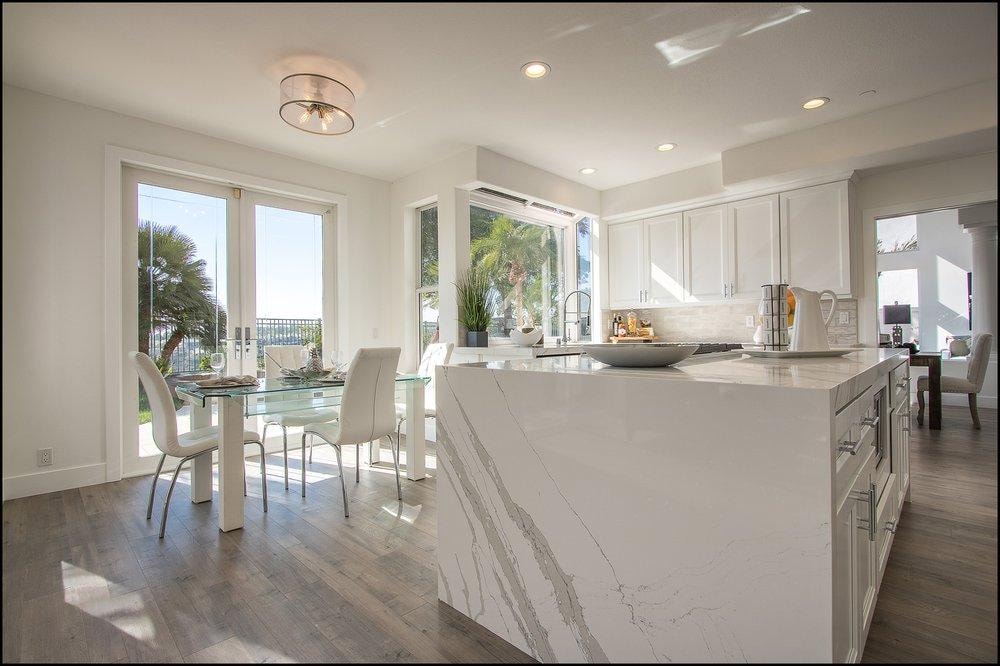 Kitchen remodel in Laguna Niguel CA — marble waterfall island, white shaker cabinets, hardwood floors, and coastal garden views by Main Street Kitchen & Flooring