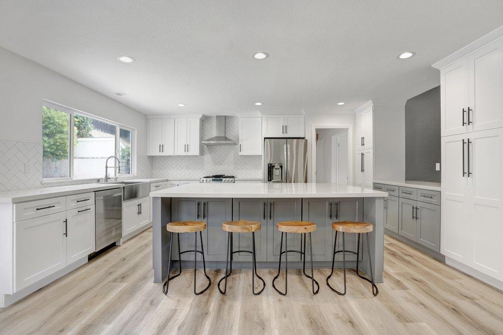 Kitchen remodel in Tustin CA — gray shaker island with quartz countertop, white shaker cabinets, herringbone tile backsplash, stainless appliances, and light wood-look vinyl plank flooring by Main Street Kitchen & Flooring